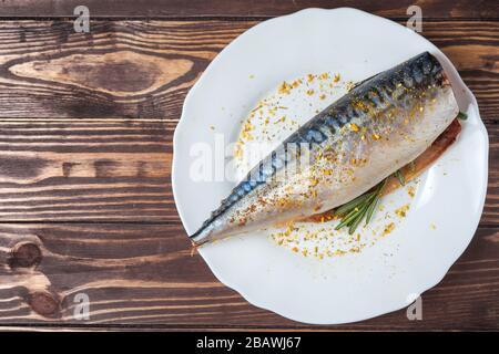 Pickled mackerel in a white plate. Raw unprepared fish. Traditional seafood delicacy, healthy eating concept. Against the background of a wooden tabletop Stock Photo