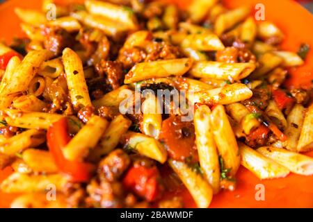 Italian pasta bolognese served on orange plate. Heaped plate of delicious Italian macaroni with tomato, fresh basil leaves and grated parmesan cheese Stock Photo