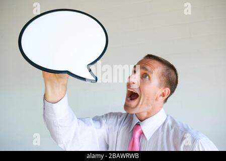 Enthusiastic businessman holding up a blank speech bubble shouting a message into copy space Stock Photo