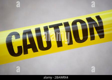 Single word CAUTION in black letters on yellow tape stretched diagonally across the frame in natural light Stock Photo