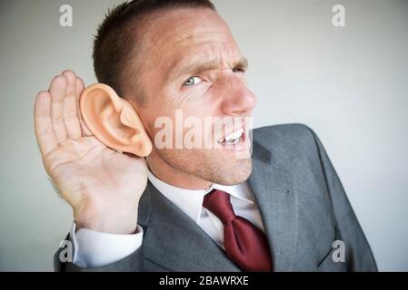 Funny businessman cupping his large ear straining to hear Stock Photo