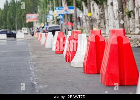 Red and white plastic barriers blocking the road for the time of repair work on the replacement of asphalt, road repair in the street in the city Stock Photo
