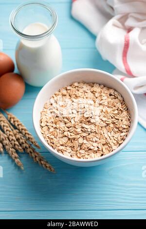 Oat flakes and bottle of milk on blue wooden table background. Ingredients for cooking oatmeal or healthy oat cookies Stock Photo