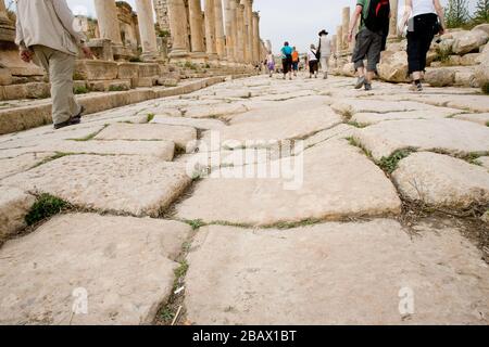 Jerash, Jordan, May 2, 2009: Tourists walk on the old uneven stone paved Colonnaded Street in the ancient city of Gerasa in Jerash, Jordan. Stock Photo