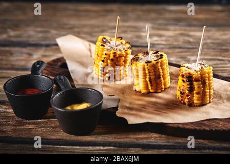 Grilled corn with sauces on a wooden background. Traditional american side dish, dark background, copy space. Stock Photo