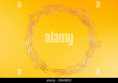 Pile of colored paper clips arranged in a circle on an orange surface Stock Photo