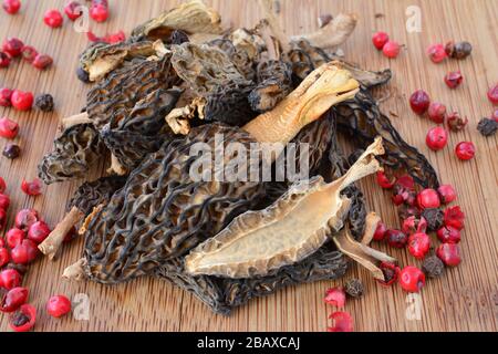 Pile of dried Morchella conica or Morel mushrooms with grains of red pepper on bamboo chopping board Stock Photo