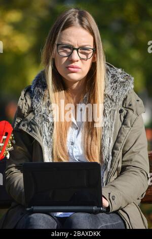 Young, beautiful, conceived blonde girl solving a problem during  work on her lap top outdoors in bright sunny autumn day Stock Photo