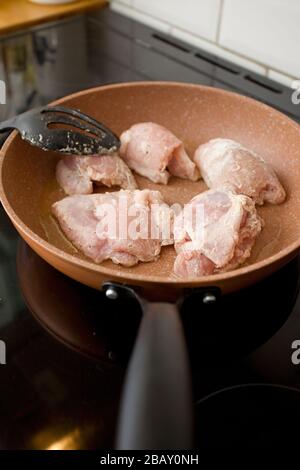 Frying raw chicken thighs in frying pan on hob Stock Photo