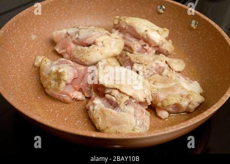 Frying chicken thighs in frying pan on hob Stock Photo