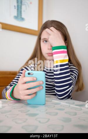 Young girl with head in hand holding her iPhone sat at the table, England Stock Photo