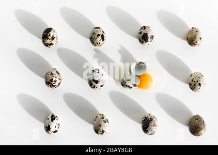 Background of small quail eggs on white table, one broken, with yellow yolk, eggshell and protein. Easter concept. Unusual paschal photo. Stock Photo