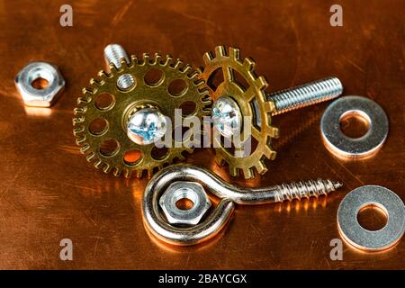 A Macro shot of several small stainless steel bolts, washers and nuts with an eyelet wood screw and various brass miniture gears, on a dirty and worn Stock Photo