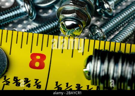 A Macro shot of the head of a small stainless steel bolt on a pile of washers, nuts and bolts, with a bright yellow tame measure strong in the frame. Stock Photo