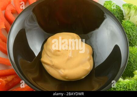 Creamy dip in black bowl with fresh raw red pepper slices and broccoli florets on plate Stock Photo