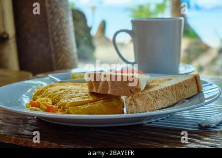 Breakfast on Boracay island of the Philippines with views of the white sandy beach and sea. An omelet and a Cup of coffee in a white dish. Stock Photo