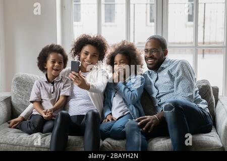 African couple with little kids making selfie seated on couch Stock Photo