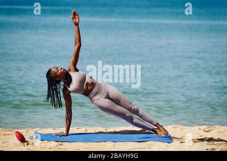 Strong woman doing side plank, outstretching arm and looking at fingers Stock Photo