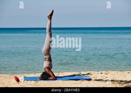 Fit slim young woman doing headstand on sandy beach in the morning Stock Photo