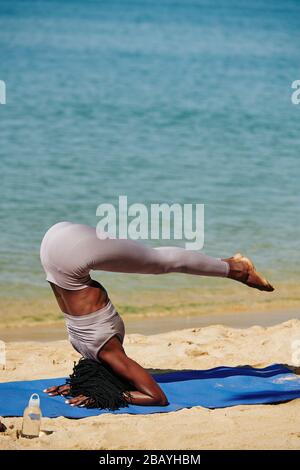 Strong fit young woman doing supported headstand on the beach Stock Photo