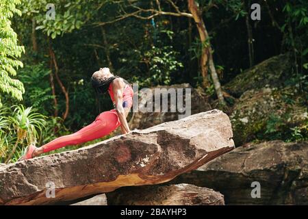 Fit beautiful Black young woman in bright orange top and leggings doing cobra asana Stock Photo