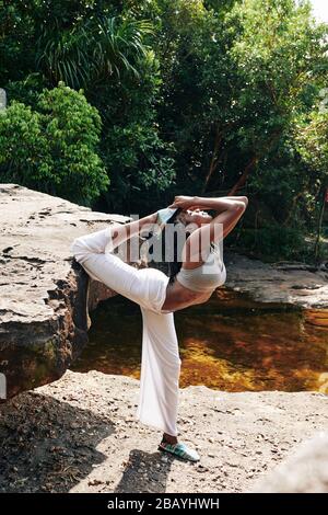 Flexible woman doing advanced yoga backbends when standing on rock in forest Stock Photo