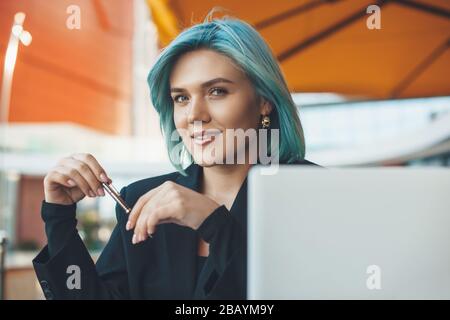 Caucasian student with blue hair working a cafeteria with a computer while looking at camera Stock Photo