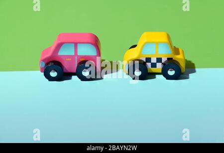 Two brightly colored wooden toy cars in pink and yellow on a divided two color green and blue background with copy space below Stock Photo