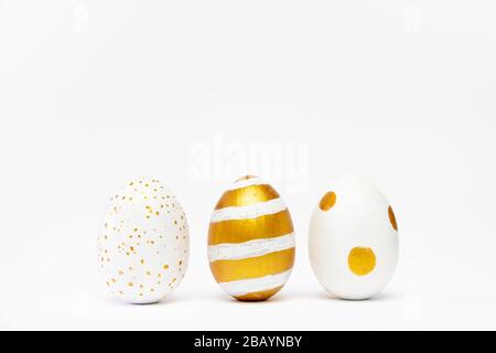 Three easter trendy golden decorated eggs on white background. Happy Easter card with copy space for text Minimal easter style Stock Photo