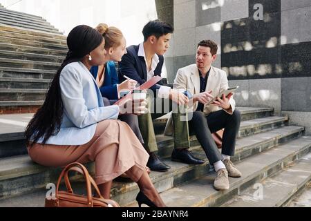 Businessman suggesting new ideas for project development when having short informal meeting with coworkers on office steps Stock Photo
