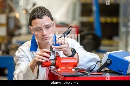 worker in metal processing plant grinds metal component on vise Stock Photo