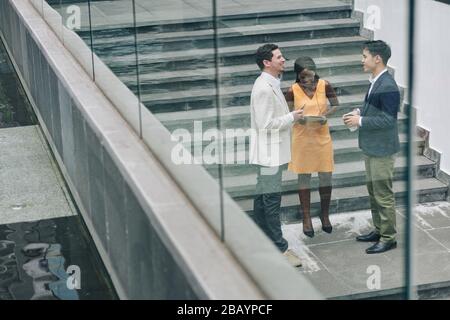Multi-ethnic group of young entrepreneurs standing on steps and discussing project details Stock Photo