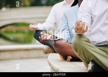 Cropped image of young business people sitting in lotus position keeping hands in shuni mudra Stock Photo