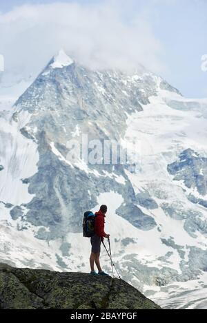 Vertical snapshot of amazing, rocky mount Ober Gabelhorn in snow in the Pennine Alps in Switzerland, located between Zermatt and Zinal, male tourist walking with hiking poles on foreground Stock Photo