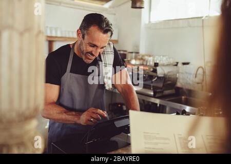Cafe owner taking order from customer at coffee shop counter. Barista entering customer order in cashbox computer. Stock Photo