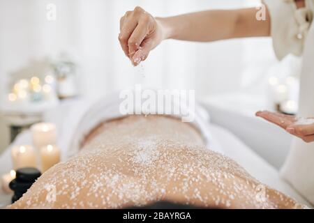 Beautician applying sea salt scrub on back of male client Stock Photo