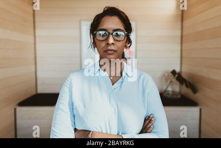 Young businesswoman standing with her arms crossed in office. Female executive in formalwear looking at camera. Stock Photo