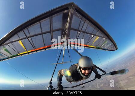 Hang glider pilot with his colorful wing flies high far away from other people. Concept of unning from crowd,self isolation and social distancing Stock Photo