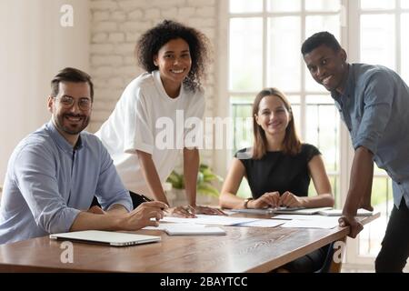 Five multiethnic businesspeople gather in boardroom smiling posing for camera Stock Photo