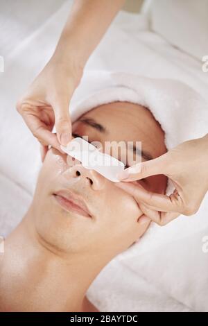 Cosmetologist applying blackhead remover sticker on nose of male client Stock Photo