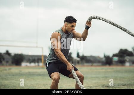 Strong man exercising with battle ropes. Athlete doing battle rope workout outdoors on a field. Stock Photo