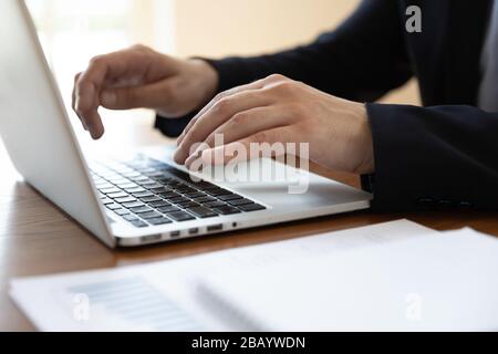 Businessman sitting at desk typing on laptop close up image Stock Photo