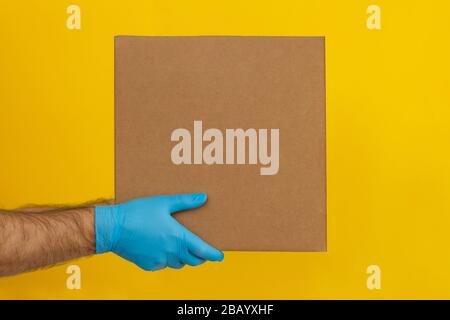 Delivery man holding cardboard boxes on yellow background. Delivery by courier in medical rubber gloves. The shipping time during coronavirus  Stock Photo