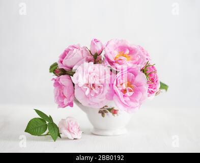 Bouquet of small light pink Roses in porcelain vase against of pale grey wooden background.  Selective focus. Shallow depth of field. Stock Photo