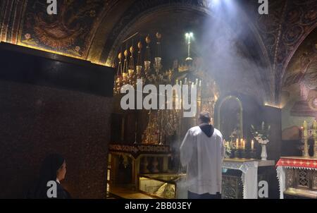 Catholic priest celebrating religious service inside the Church of the Holy Sepulchre. The Rock of Calvary can be seen under the glass. Jerusalem Stock Photo