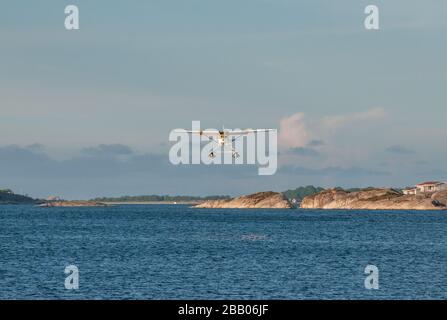 A yellow and white Cessna 172 Skyhawk seaplane taking off among islands in the Kragerø archipelago on south coast of Norway. Stock Photo