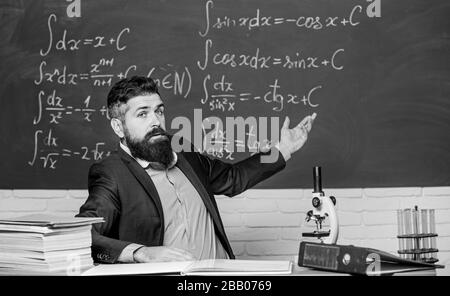 Talking to students or pupils. School teacher concept. Teacher bearded man tell interesting story. Teacher charismatic hipster sit at table classroom chalkboard background. Educational conversation. Stock Photo