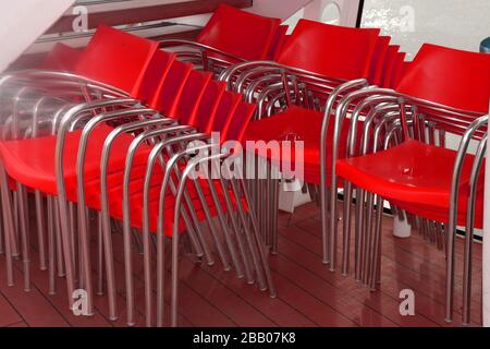 stacked red colored chairs in boat with light reflections, empty stacked chairs on board of ferry boat Stock Photo