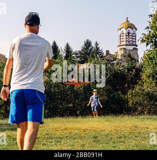 Caucasian Father and son happy and enjoying playing together and learning to fly model airplane glider in village park.Bulgaria Stock Photo