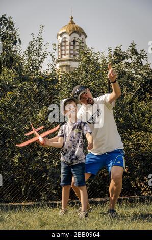 Caucasian Father and son happy and enjoying playing together and learning to fly model airplane glider in village park.Bulgaria Stock Photo